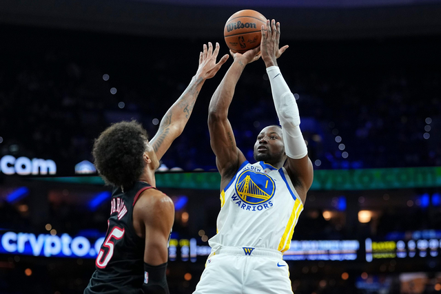 A Golden State Warriors player jumps to shoot a basketball while a defender wearing number 5 reaches up to block the shot during a game.